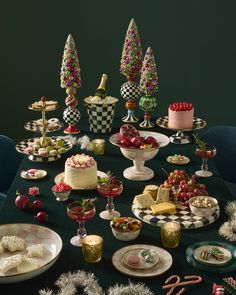 a table topped with cakes and desserts covered in frosting next to christmas trees