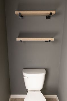 a white toilet sitting in a bathroom next to two wooden floating shelves on the wall