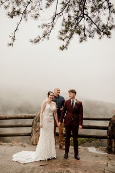 a bride and groom holding hands while standing next to each other on top of a mountain