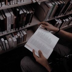 a person sitting on the floor reading a book in front of a bookshelf