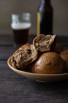 a bowl filled with muffins next to a bottle of beer on top of a wooden table