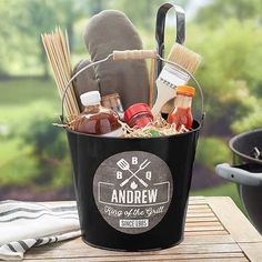 an outdoor bbq basket with barbecue accessories and sauces in it on a picnic table