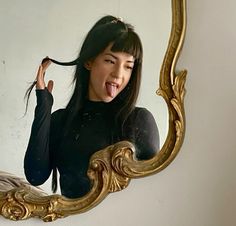 a woman sticking her tongue out in front of a mirror with an ornate gold frame