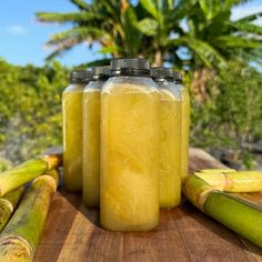 three jars filled with yellow liquid sitting on top of a wooden table next to bananas