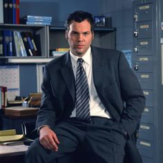 a man in a suit and tie sitting on a chair next to a filing cabinet