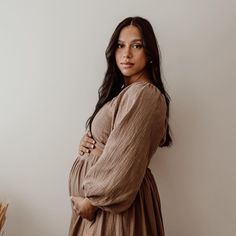 a woman standing in front of a white wall with her arms crossed and looking at the camera