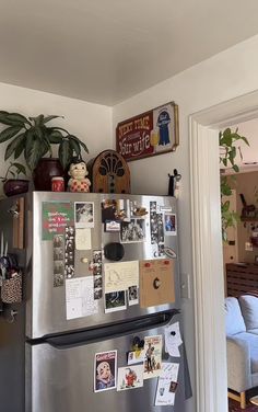 a refrigerator covered in magnets and pictures next to a couch with a potted plant on top