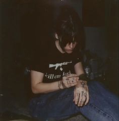 a person sitting on the ground with their hands in their pockets and tattoos on their arms