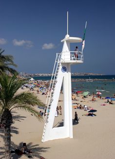 a lifeguard tower on the beach with people swimming in the water and palm trees