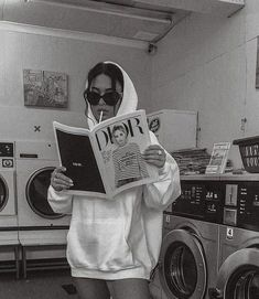 a woman reading a magazine while standing in front of washing machines