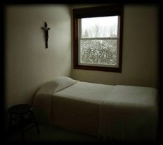 a small bedroom with a cross hanging on the wall and a bed in front of a window