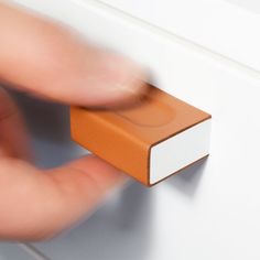 a close up of a person's hand holding an orange object on a white surface