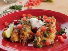 a red plate topped with two enchiladas covered in sour cream and garnish