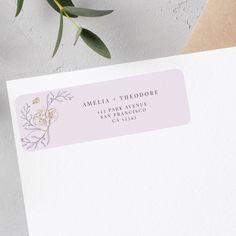 a close up of a white envelope with a pink flower on it and a green plant in the background