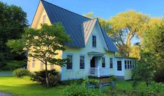 a yellow house with a blue roof in the middle of some trees and bushes near a road