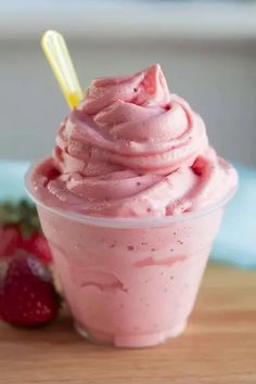 a cup filled with pink frosting next to strawberries