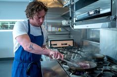 a man cooking food on top of a frying pan in front of an oven