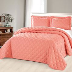 a bed with pink comforter and pillows in a room next to a white dresser