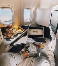 a person sitting in an airplane with their feet up on the bed while using a laptop