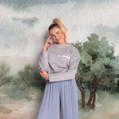 a woman standing in front of a painting wearing blue pants and a grey sweater with the words,