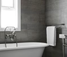 a white bath tub sitting under a window next to a sink and towel rack in a bathroom