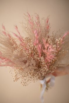 a person holding a bunch of flowers with pink stems and white ribbons on it's wrist