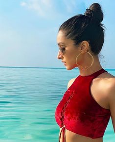 a woman standing in the ocean wearing a red top and gold hoop earrings