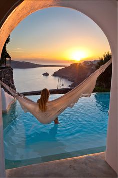 a woman sitting in a hammock next to a swimming pool at sunset with the sun setting