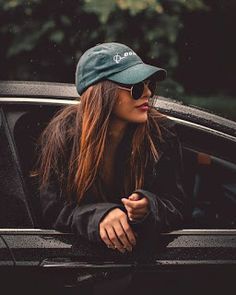 a woman in sunglasses and a hat leaning out the window of a car with her hand on her hip