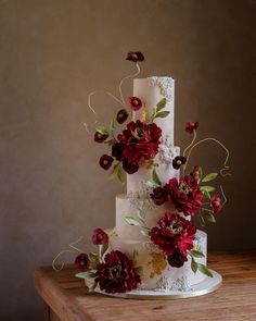 a three tiered white cake with red flowers on the top and bottom, sitting on a wooden table