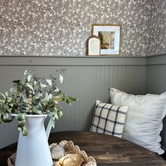 a white vase with flowers sitting on top of a wooden table next to a pillow