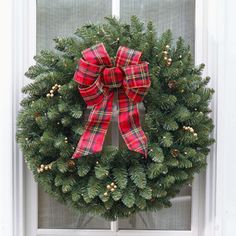 a christmas wreath on the front door with red and green plaid bow hanging from it