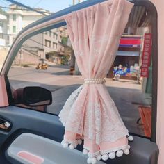 a pink curtain hanging from the side of a car window with pom poms