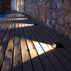 the sun shines on a wooden deck next to a swimming pool and stone wall