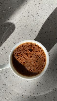 a cup of coffee is sitting on a table with the shadow of a person's hand