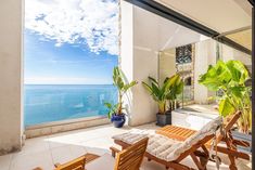 a balcony overlooking the ocean with wooden chairs and potted plants in front of it