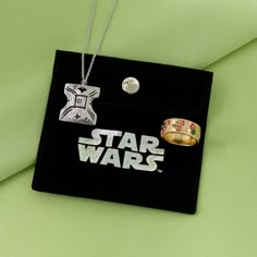 a star wars necklace and ring are on a black box with a green fabric behind it