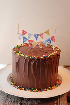 a chocolate birthday cake with sprinkles and bunting on the top is sitting on a white plate