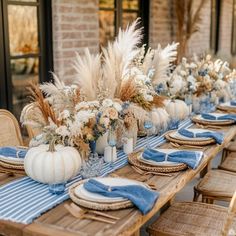 a table set with blue and white place settings, pumpkins and pamonini