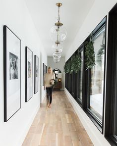 a woman walking down a long hallway with pictures hanging on the wall and plants in vases