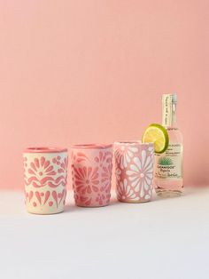 three shot glasses sitting next to each other on a white surface with a pink wall in the background