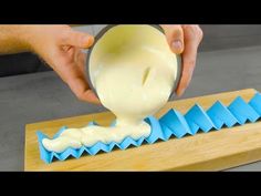 a person pouring cream into a bowl on top of a cutting board with blue origami shapes