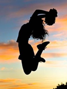 a person jumping in the air while holding onto a skateboard at sunset or dawn