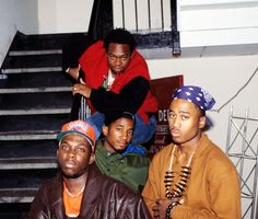 four young men sitting on the stairs in front of a staircase case, one is wearing a red shirt and the other wears a black jacket