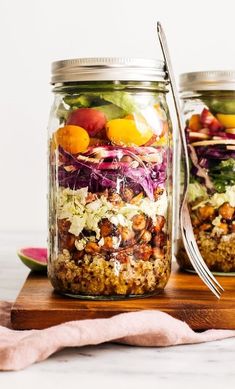 two mason jars filled with salad on top of a wooden cutting board