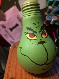 a green vase with an angry face painted on it's side sitting on a wooden table