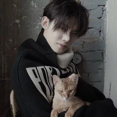 a man holding a cat in his arms while sitting on a chair next to a brick wall