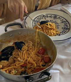 a person is eating spaghetti with clams and mussels in a large pan