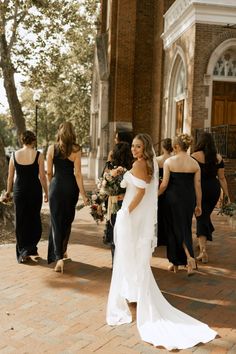 a bride and her bridesmaids walking down the street in front of an old church