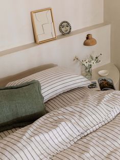 a bed with striped sheets and pillows next to a framed photograph on the wall above it